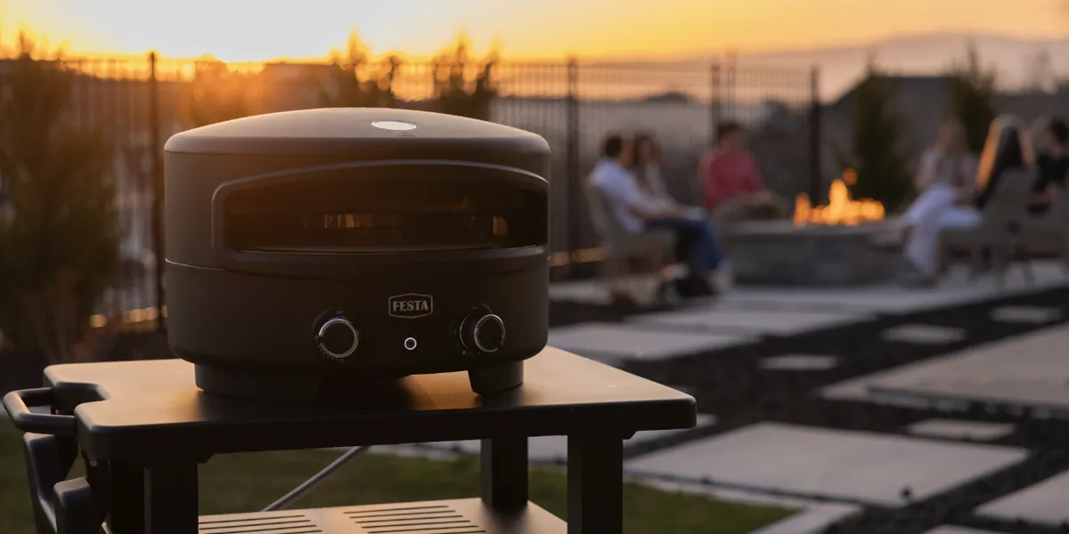 Festa Pizza Co Dual-Heat Rotating Pizza Oven, on an outdoor cart on a patio at sunset
