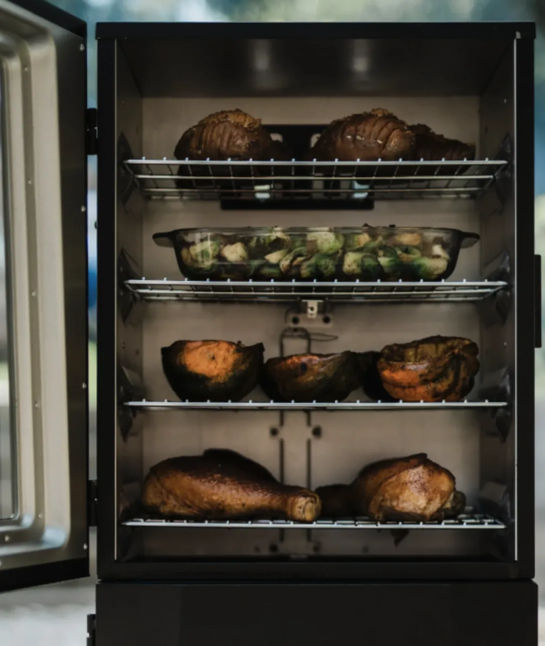 Masterbuilt 40" ThermoTemp XL Propane Smoker, door open showing four racks of turkey legs, squash, Brussels sprouts and hasselback potatoes