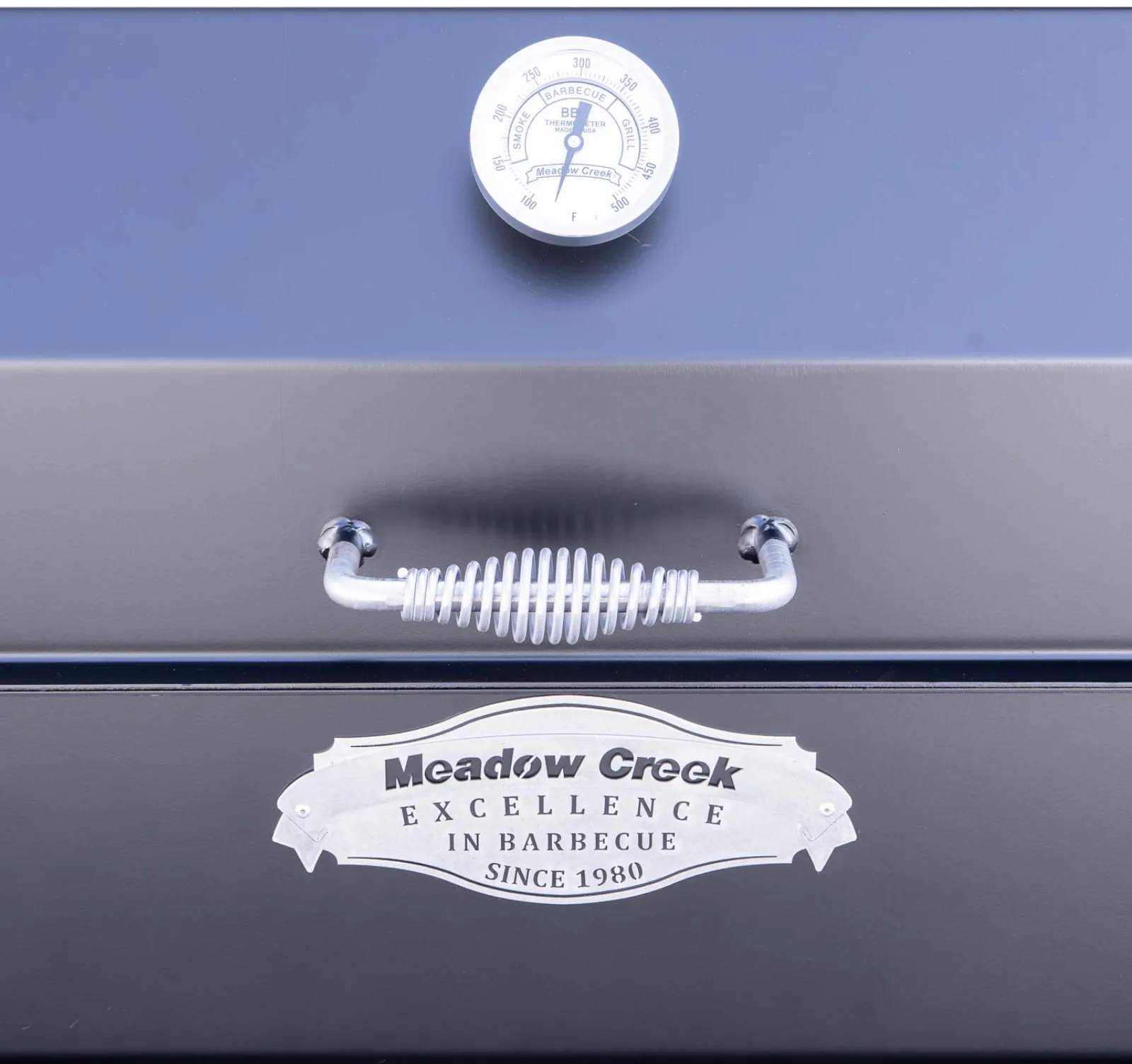 Close-up of Meadow Creek SQ36 smoker lid with temperature gauge, spring handle, and Meadow Creek badge.