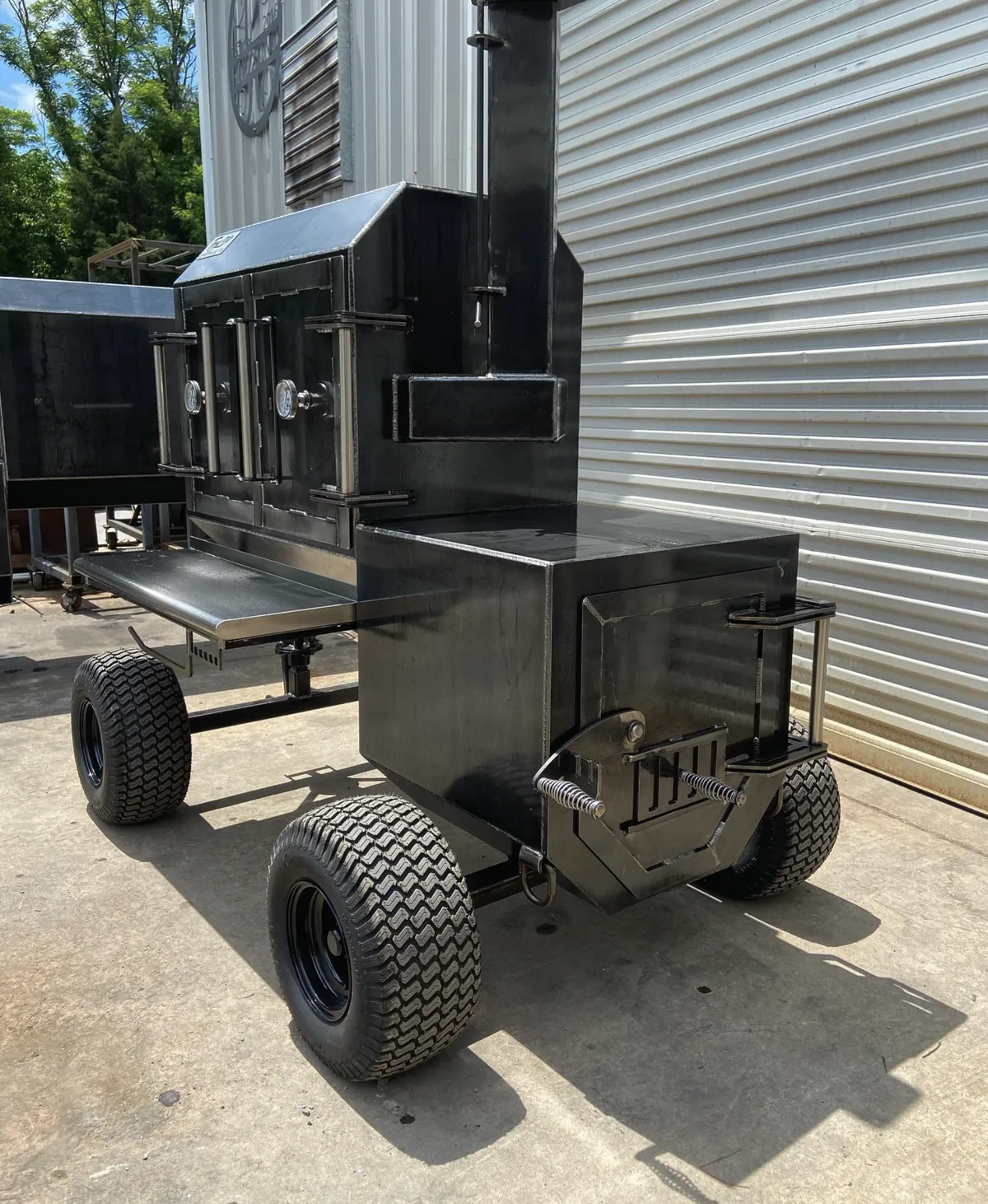 TMG Pits The Fridge Cabinet Smoker, rear view showing the firebox door and smokestack on turf tires
